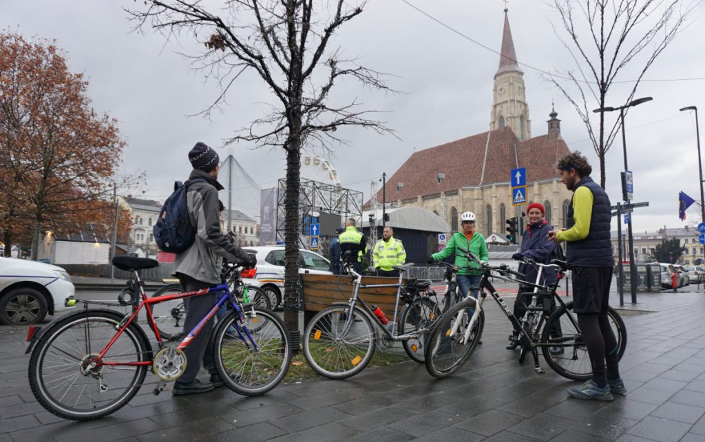 Kerékpáros gyülekező 2022 utolsó critical mass-én Kolozsváron. Hideg, nedves az idő, ezért mintegy tucatnyian gyűlnek össze a Centrul pentru Cicloturism Napoca (CCN) által szervezett eseményre. A háttérben a helyi rendőrség várakozik – indulás előtt rövid tanakodás után az a döntés születik, hogy nem szükséges a rendőri kíséret.